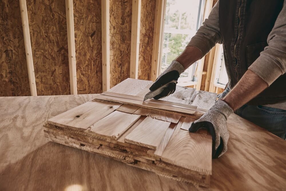 Photo of STANLEY 10-099 utility knife cutting wood in a workshop, close-up of hands wearing gloves.