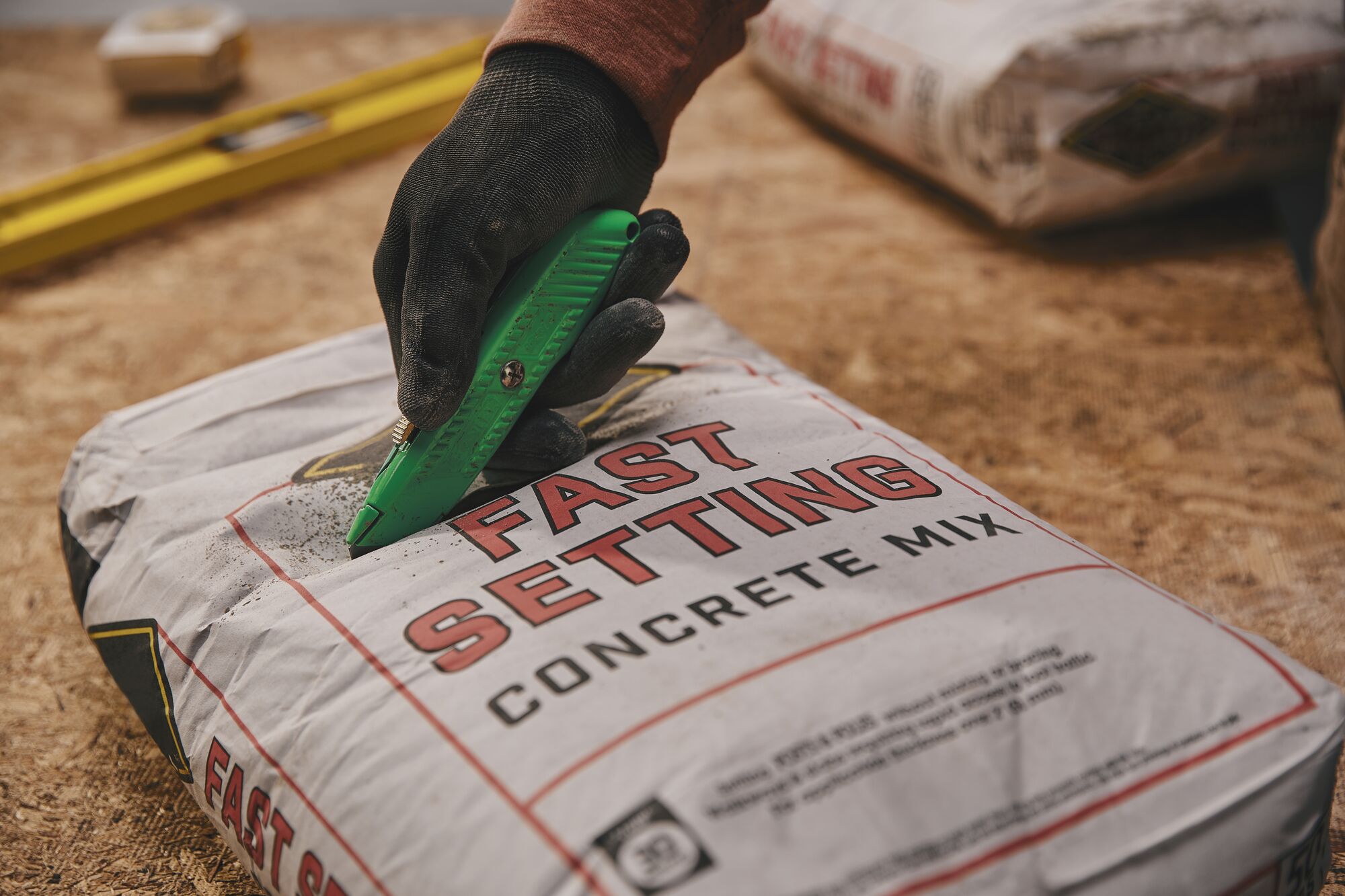 STANLEY 10-179 utility knife cutting concrete mix bag, hand in black glove holding knife, close-up.