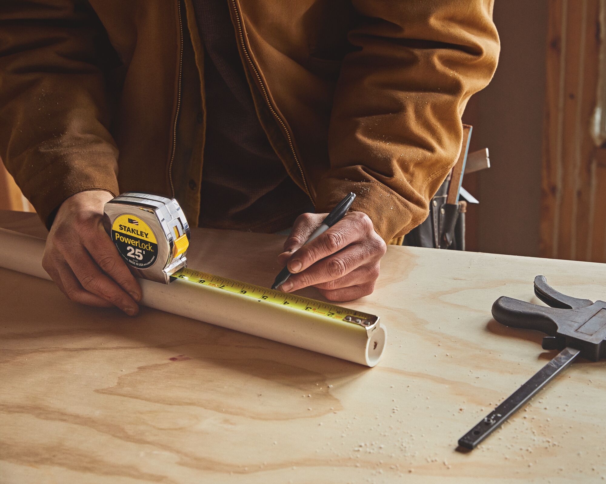 Stanley 33-425 PowerLock tape measure marking PVC pipe on workbench, photography close-up.