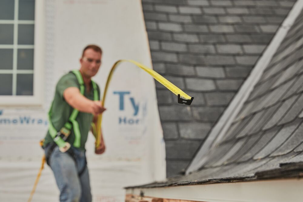 STANLEY 33-725 tape measure extended by a worker in a harness next to a sloped roof, construction setting.
