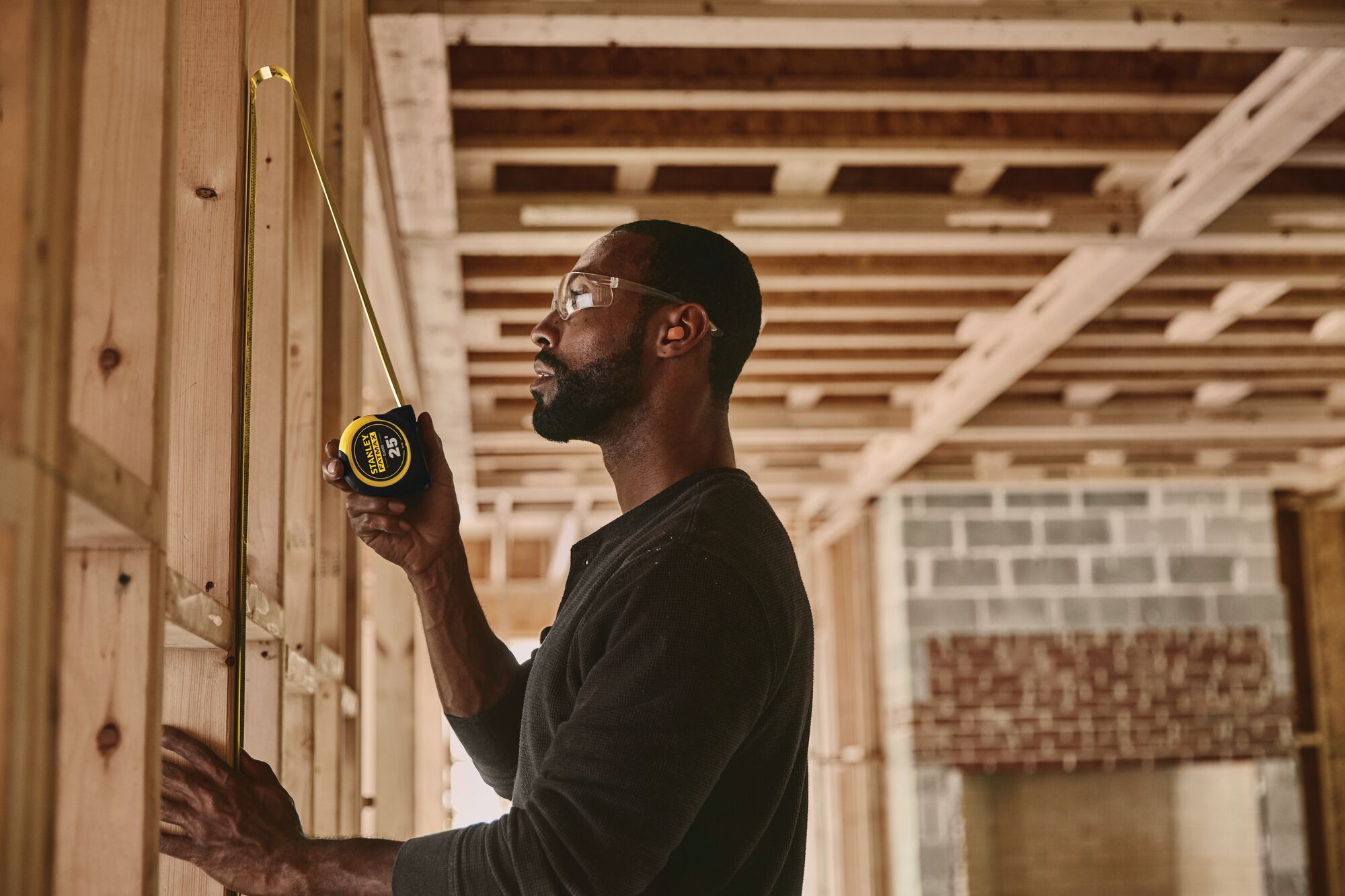 STANLEY 33-725 tape measure used to measure wooden studs in a construction framing setting.