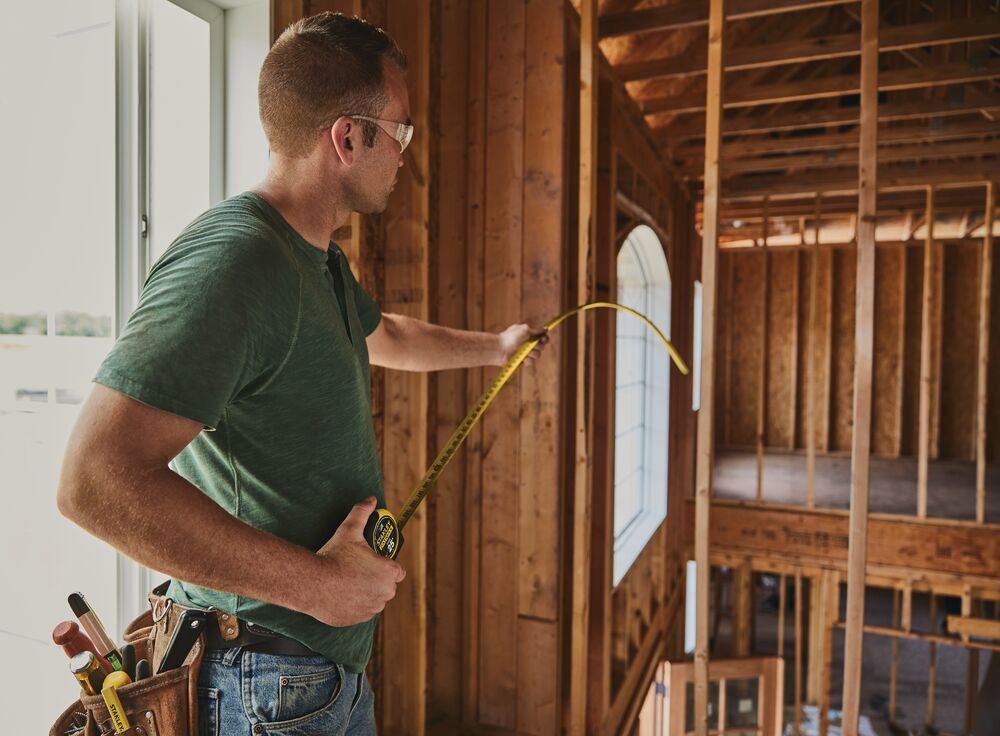 STANLEY 33-725 tape measure in use at a construction site, held by a person measuring a wooden frame wall.
