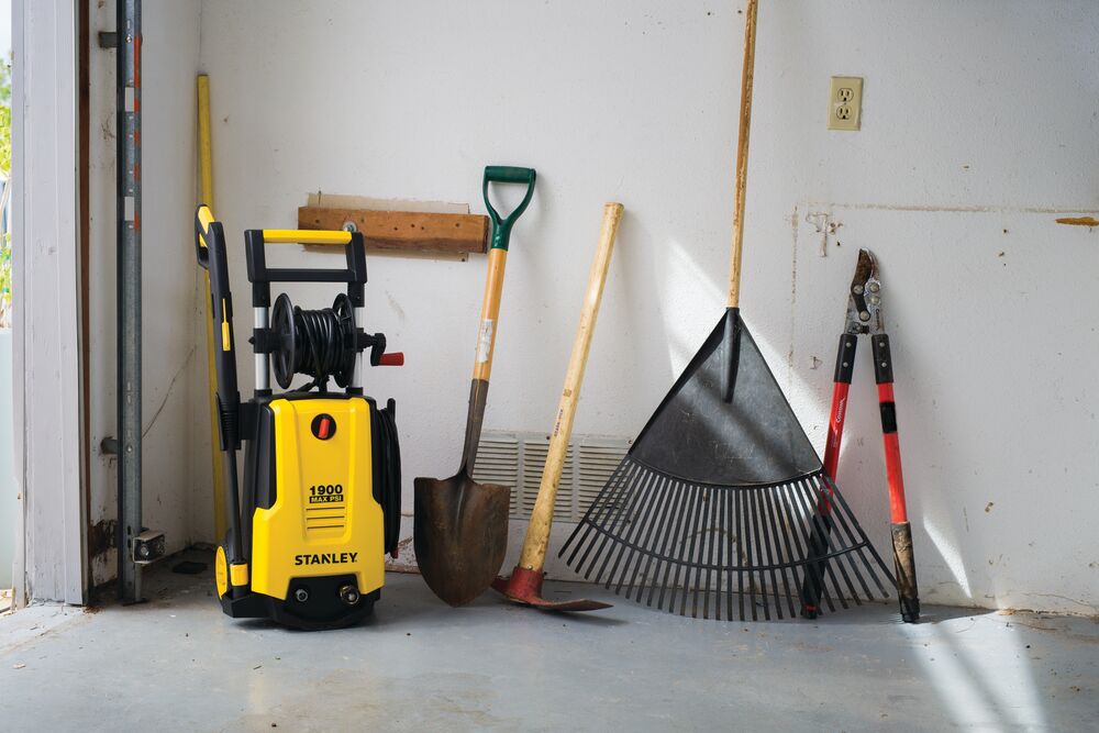 Photo of STANLEY SHP2150 yellow pressure washer, front angle, beside garden tools in a garage.