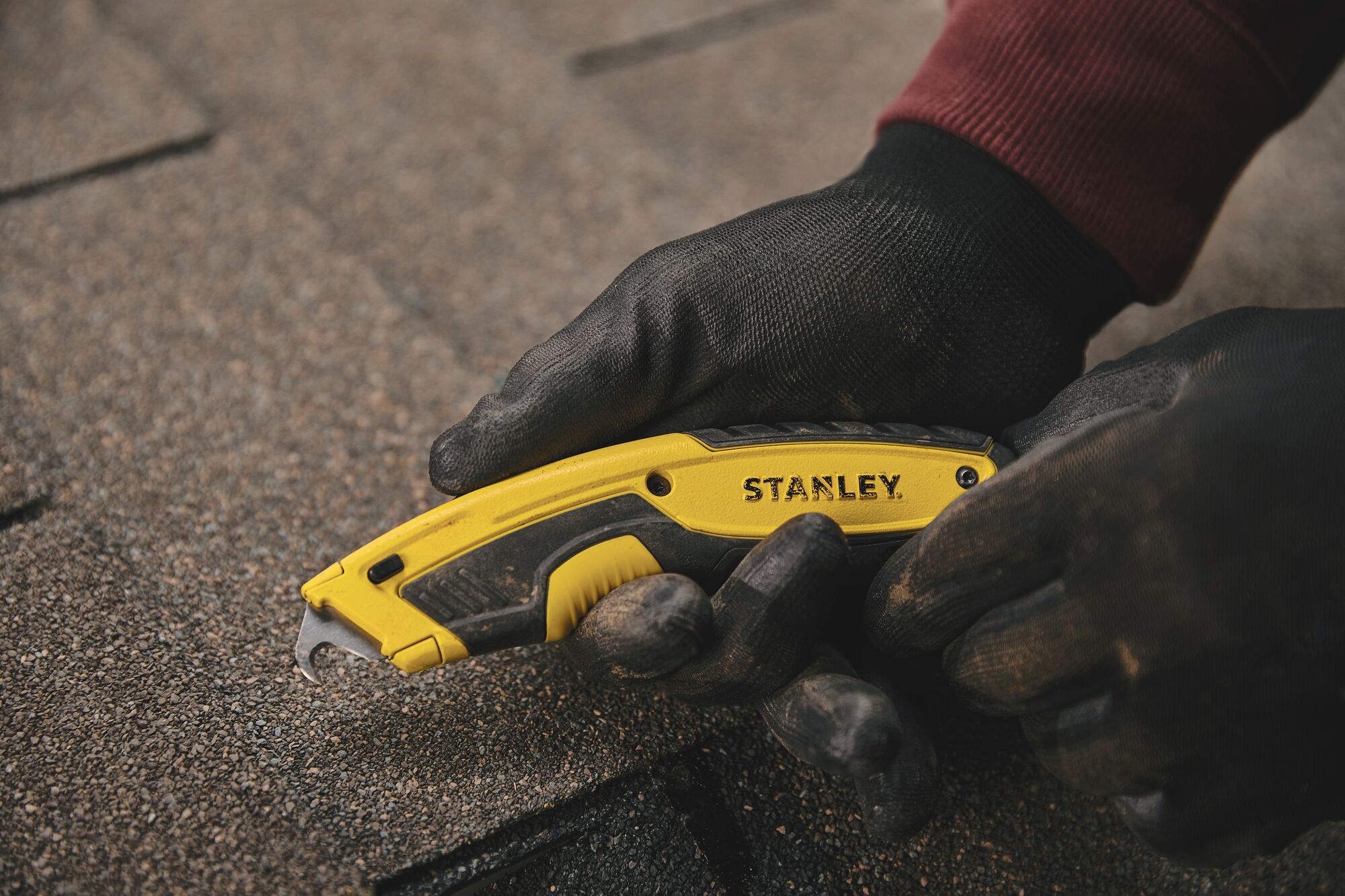 Photo of STANLEY STHT10479 utility knife in use, yellow and black handle, cutting roofing shingles.
