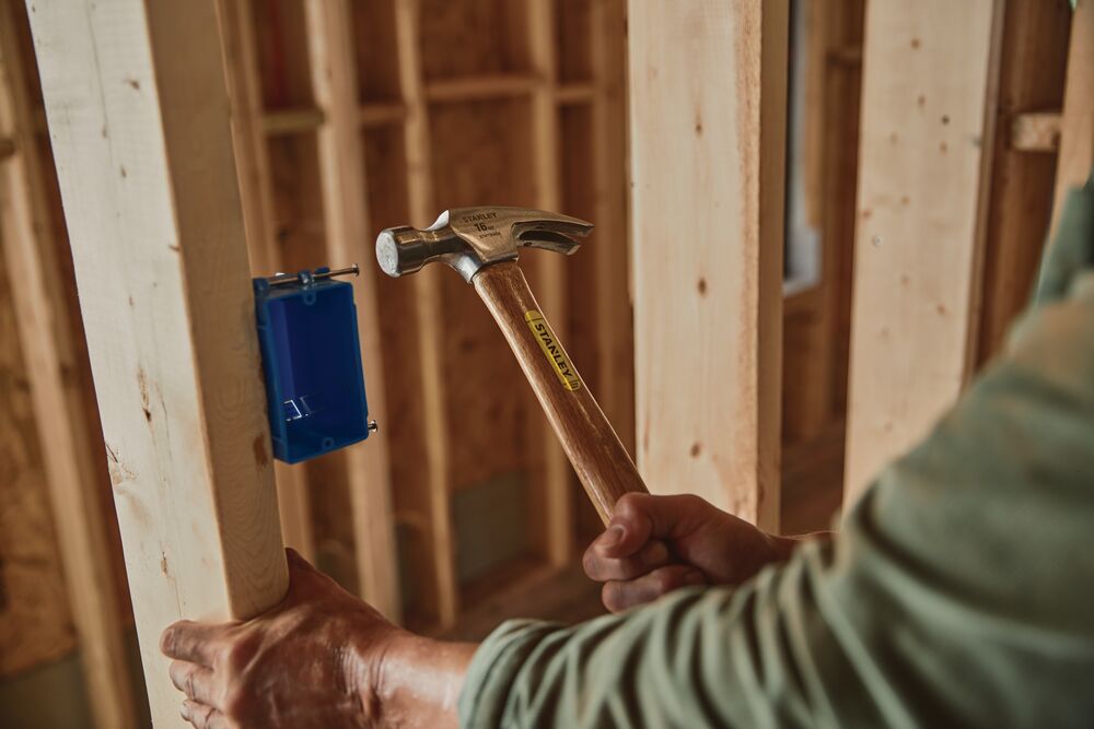 STANLEY STHT51456 claw hammer with wooden handle being used on a construction site.