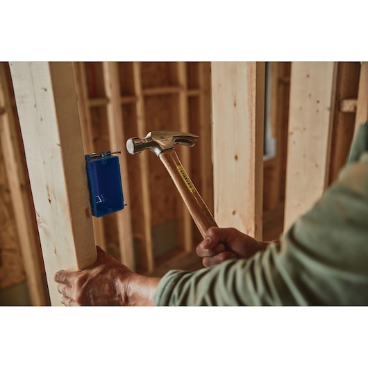 STANLEY STHT51456 claw hammer with wooden handle being used on a construction site.